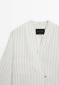 Blazer blanc à fines rayures verticales noires, col en V profond, fermeture à un bouton, coupe ample et détail de poche poitrine.