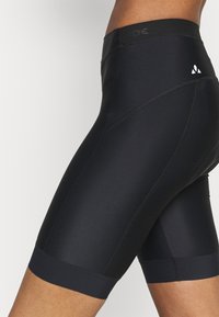 Lähikuva henkilöstä, joka käyttää mustia urheilukompressioshortsseja, joissa näkyy tikkaus ja pieni valkoinen logo sivulla.