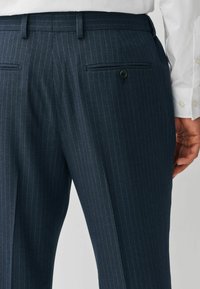 Marineblaue Nadelstreifen-Hosen mit maßgeschneidertem Schnitt, ausgestattet mit einer glatten Textur, Gürtelschlaufen und zwei Gesäßtaschen mit Knopfverschluss.