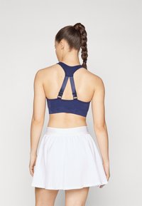 Sujetador deportivo azul marino con diseño de espalda de nadadora, correas ajustables y una textura suave, combinado con una falda acampanada blanca.