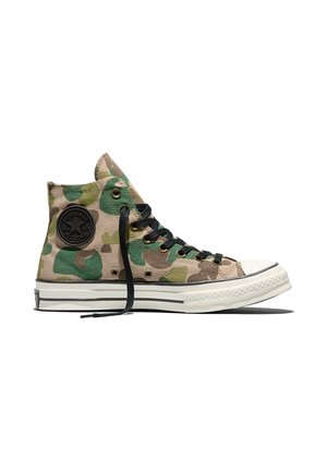 Baskets montantes en toile avec imprimé camouflage vert et marron, lacets noirs, semelle blanche en caoutchouc et écusson rond noir avec le logo Converse.