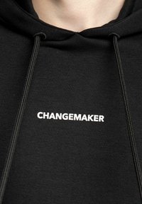 Czarna bawełniana bluza z kapturem, z sznurkiem i napisem "CHANGEMAKER" w kolorze białym na przodzie. Gładka tekstura, casualowy design.