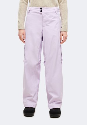 Modèle portant un pantalon cargo lavande clair à jambes larges, avec deux boutons noirs à la taille et des chaussures noires.