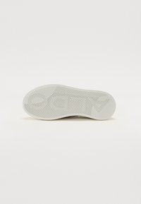 Sål av en sko, gummimateriale, hvit farge, med et fiskebensmønster og preget logo. Glatt tekstur med lett krumning.