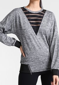 Pullover grigio a maniche lunghe con inserto in rete nera a forma di V, caratterizzato da un design a righe, polsini a coste e dettagli laterali con zip.