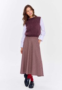 Burgundská bezrukávová svetrová mikina na bielej košeli, doplnená plisedovanou sukňou s červeným a čiernym károm. Čierne platformové topánky dotvárajú tento outfit.