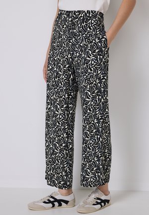Weite Hosen in Schwarz und Creme mit einem Blattmuster. Ausgestattet mit einem elastischen Bund und seitlichen Taschen. Kombiniert mit lässigen Sneakers.