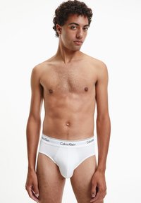 Slip bianchi in cotone con una morbida fascia in vita, caratterizzati dal logo "Calvin Klein" in nero. Il design è minimalista e aderente.