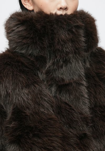 Rudas dirbtinio kailio paltas su aukštu apykakle, tankia tekstūra ir skirtingais rudais atspalviais, su švelniu žvilgesiu. Nėra matomų detalių ar raštų.