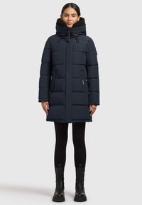 Mørkeblå dunjakke med høj krave, polstret design og to sidelommer. Jakken har en frontlynlås og er lavet af glat stof.