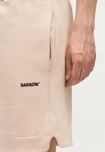 Μπεζ σορτς με πλαϊνή τσέπη και λογότυπο "BARROW", εμφανίζονται δίπλα σε χαλαρό χέρι σε απλό φωτεινό φόντο.