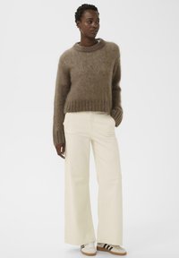 Pull brun duveteux avec un col rond et des poignets côtelés, associé à un pantalon large crème et des baskets à rayures noires.