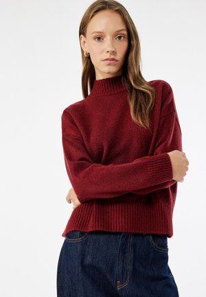 Bordeaux strikket sweater med høj krave, ribbede mansjetter og kant. Blød tekstur, løs pasform, parret med mørke jeans.