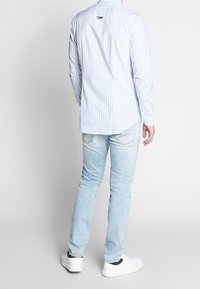 Camicia a maniche lunghe a righe blu chiaro e bianche con polsini bottonati, abbinata a jeans blu chiaro sbiaditi e sneakers bianche.
