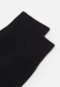 Calze nere lavorate a maglia con una texture liscia, caratterizzate da un bordo superiore a coste e un design semplice. Materiale morbido, adatto per un abbigliamento informale.