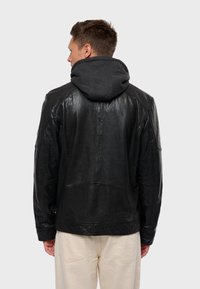 Chaqueta de cuero negra con un acabado texturizado, que presenta una capucha gris desmontable y detalles de costura, vista desde atrás.