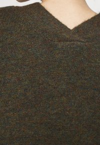 Brun texturerad stickad tröja med V-ringning, med varierande nyanser inklusive inslag av grön och blå, samt ribbad halsringning.