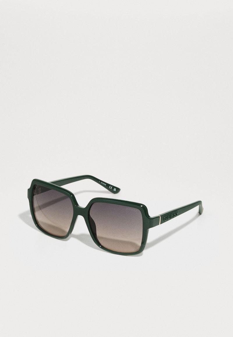 Green plastic sunglasses with a square frame, gradient brown lenses, and embossed logo on the arm. Smooth texture with polished finish.