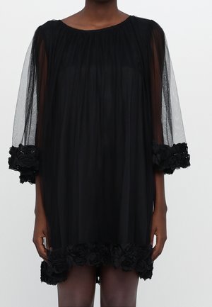 Czarna przezroczysta sukienka z długimi rękawami z siateczki i haftowanymi kwiatowymi akcentami na mankietach i u dołu. Miękka, płynąca sylwetka.