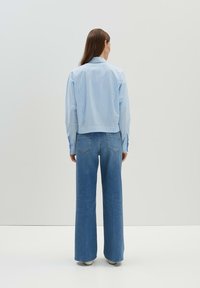 Hellblau gestreiftes, kurzes Hemd mit langen Ärmeln, kombiniert mit hoch taillierten, weit geschnittenen blauen Jeans. Einfaches Design, glatte Textur.