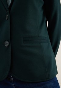 Donkergroen blazer van zachte stof, met een enkele knoopsluiting, een reverskraag en een zijzak.