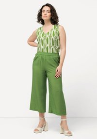 Groene cropped broek met elastische tailleband, gecombineerd met een mouwloos topje met groen-witte print. Gekenmerkt door platte sandalen met dikke, lichtgekleurde hakken.