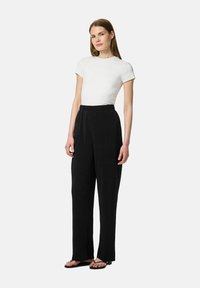 Pantalons larges noirs avec une finition texturée, une taille élastique, associés à une chemise blanche ajustée à manches courtes et des sandales.