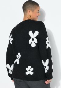 Zwarte gebreide trui met grote witte bloemmotieven, een losse pasvorm en geribbelde manchetten. Getextureerde stof met een ronde hals.