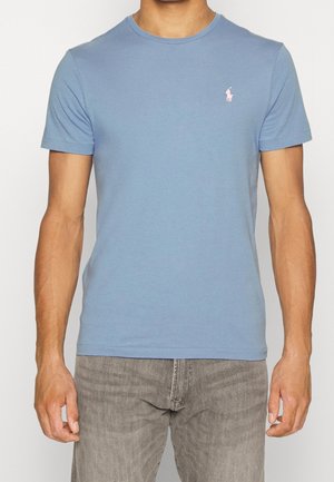 Camiseta de algodón azul claro con cuello redondo, mangas cortas y un pequeño logo rosa bordado en el lado izquierdo del pecho.