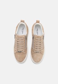 Baskets en daim beige avec une finition texturée, dotées de fermetures éclair en métal, de lacets et d'une semelle en caoutchouc blanc, affichant un design minimaliste.