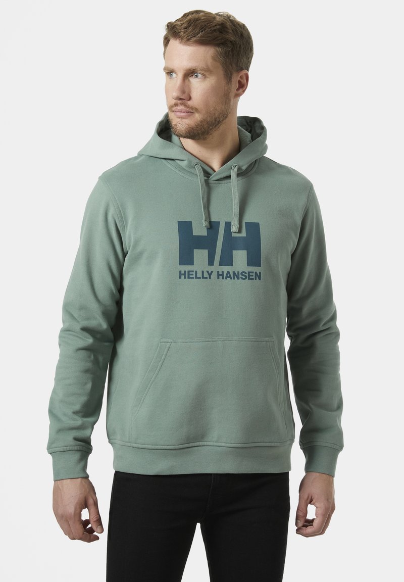 Sudadera verde hecha de tela suave, con un bolsillo tipo canguro y cordones ajustables. Gran logo azul de Helly Hansen impreso en la parte frontal.
