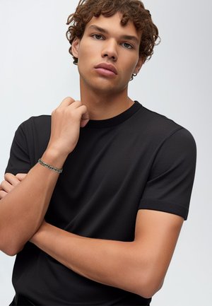Black short-sleeve t-shirt with a round neckline, smooth fabric, and ribbed cuffs; worn by a person with light skin and curly hair.