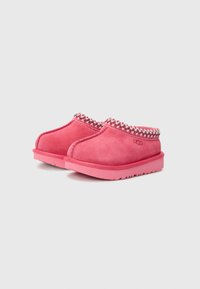 Rosafarbene Wildlederschlappen mit einem strukturierten Kragen, der ein gewebtes Muster aufweist. Die Sohle ist pink, rund und leicht erhöht. UGG-Logo sichtbar.