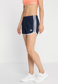 Marinaidrottsshorts med vita sidostreck, avslappnad passform och elastisk midja. Tillsammans med vita sneakers och en rosa sport-bh.