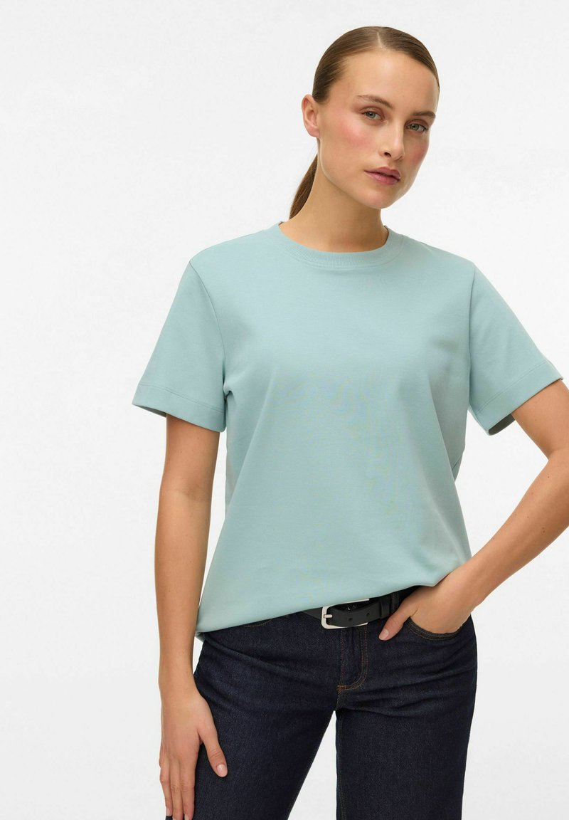 Lichtblauw katoenen T-shirt met een ronde hals en korte opgerolde mouwen, gecombineerd met een donkere spijkerbroek met een zwarte riem en zilverkleurige gesp.