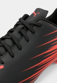 Μαύρο ποδοσφαιρικό παπούτσι με κόκκινο σχέδιο γραμμών, μαύρα κορδόνια και κόκκινο λογότυπο Puma στη γλώσσα, εμφανιζόμενο σε κοντινή λήψη.