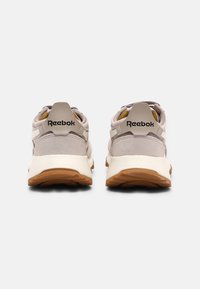 Grå Reebok-sneakers med ovandel i mocka och mesh, vit mellansula och brun gummisula. Har logotyp på hälen och gula detaljer inuti.