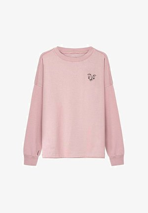 Jasnoróżowa koszula z długim rękawem, o okrągłym dekolcie, z małym czarnym abstrakcyjnym wzorem twarzy na lewej piersi i nadgarstku.