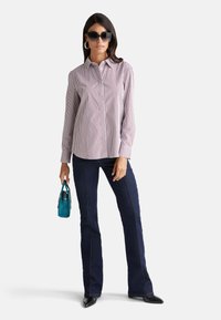 Camicia a righe con colori chiari e scuri, abbinata a jeans svasati scuri. Gli accessori includono una piccola borsa a tracolla color turchese e occhiali da sole.