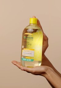 Garnier Micellar Cleansing Water-flaska, 700 ml, klar vätska, gul kork, märkt med grön och gul text, hålls i en hand. Vegansk formel.