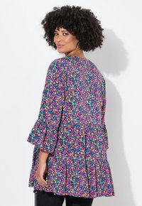 Tunika floreale con maniche lunghe e svasate, caratterizzata da un motivo rosa e blu su uno sfondo blu navy e una vita arricciata.