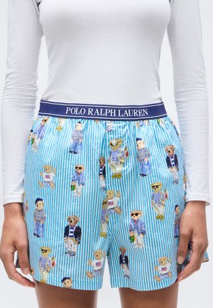 Shorts rayés bleu et blanc avec une ceinture Polo Ralph Lauren ornée d'ours en peluche vêtus de différentes tenues. Chemise blanche à manches longues rentrée à l'intérieur.