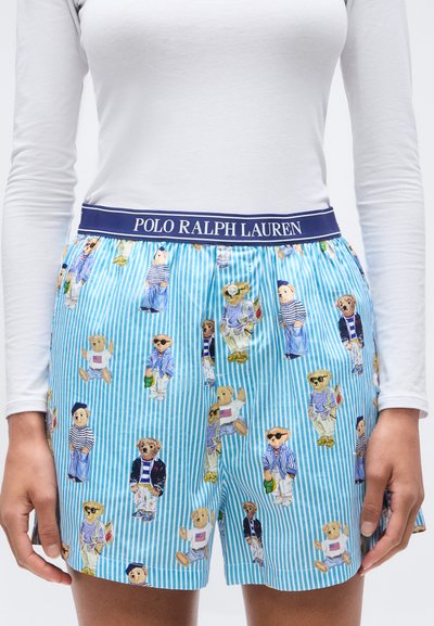 Blå och vitrandiga shorts med Polo Ralph Laurens midjeband med nallar i olika kläder. Vit långärmad skjorta instoppad.