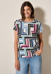Haut à manches courtes multicolore présentant des motifs géométriques en noir, bleu, rose et vert, fabriqué en tissu doux et léger.