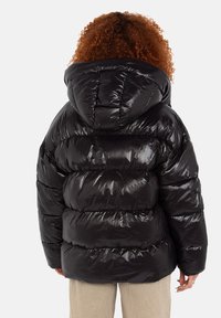 Sort pufferjakke med en blank tekstur, oversized hætte og vandrette quiltede sektioner. Har elastiske manchetter og en afslappet pasform.