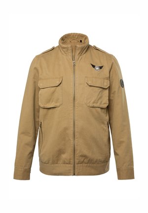 Khaki jakke med høj krave, frontlynlås, to brystlommer og et emblem på venstre skulder. Materialet er bomuld med en glat tekstur.