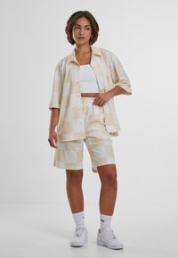 Chemise à manches courtes avec boutons et short assorti en beige clair et blanc à carreaux, fabriqués en tissu lisse, avec taille élastique et poches latérales.