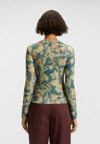 Long-sleeve top with a floral print in green, yellow, and peach colors. Made of a lightweight, sheer material with a fitted design.