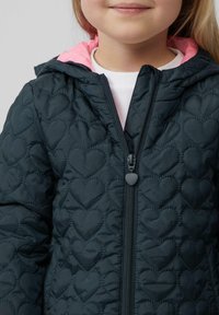 Gequilted marineblauwe jas met hartpatronen, roze voering in de capuchon en een rits aan de voorkant met een hartvormige trekker.