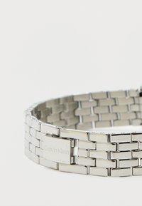 Ezüst rozsdamentes acél karkötő téglalap alakú láncszemekkel, fényes felülettel és gravírozott "Calvin Klein" logóval a csattón.